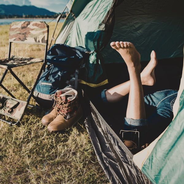 Person lying inside a tent with camping gear and a chair outside, near a lake.