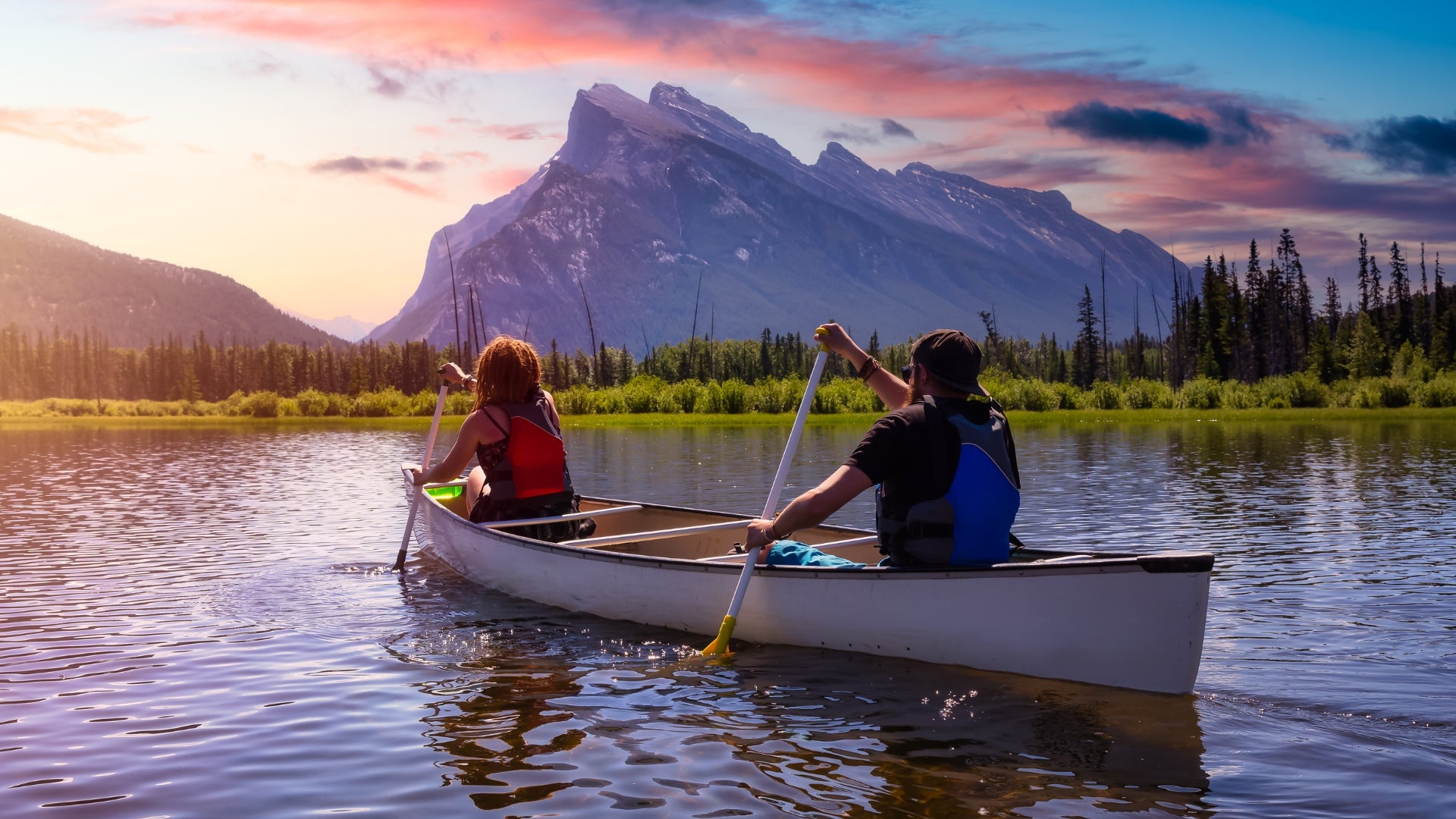 Two people paddling a canoe on a lake with mountains in the background