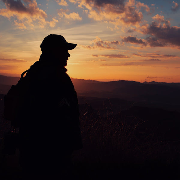 Silhouette of a hiker with backpack watching a vibrant orange sunset over mountains
