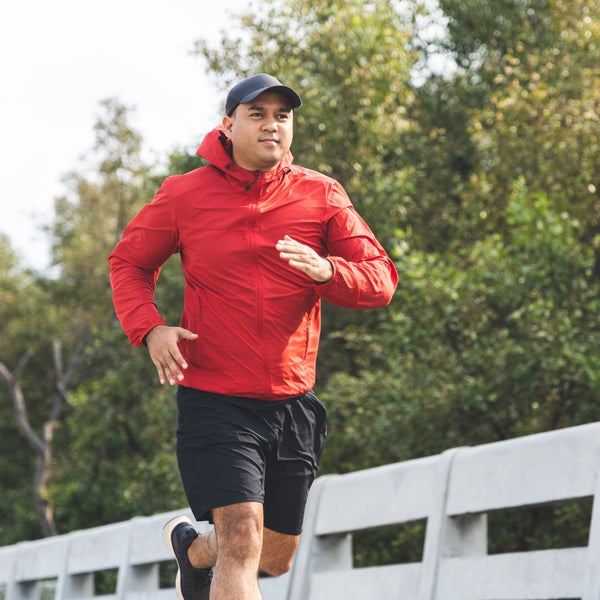 Man in a red jacket running on a bridge with green trees in the background