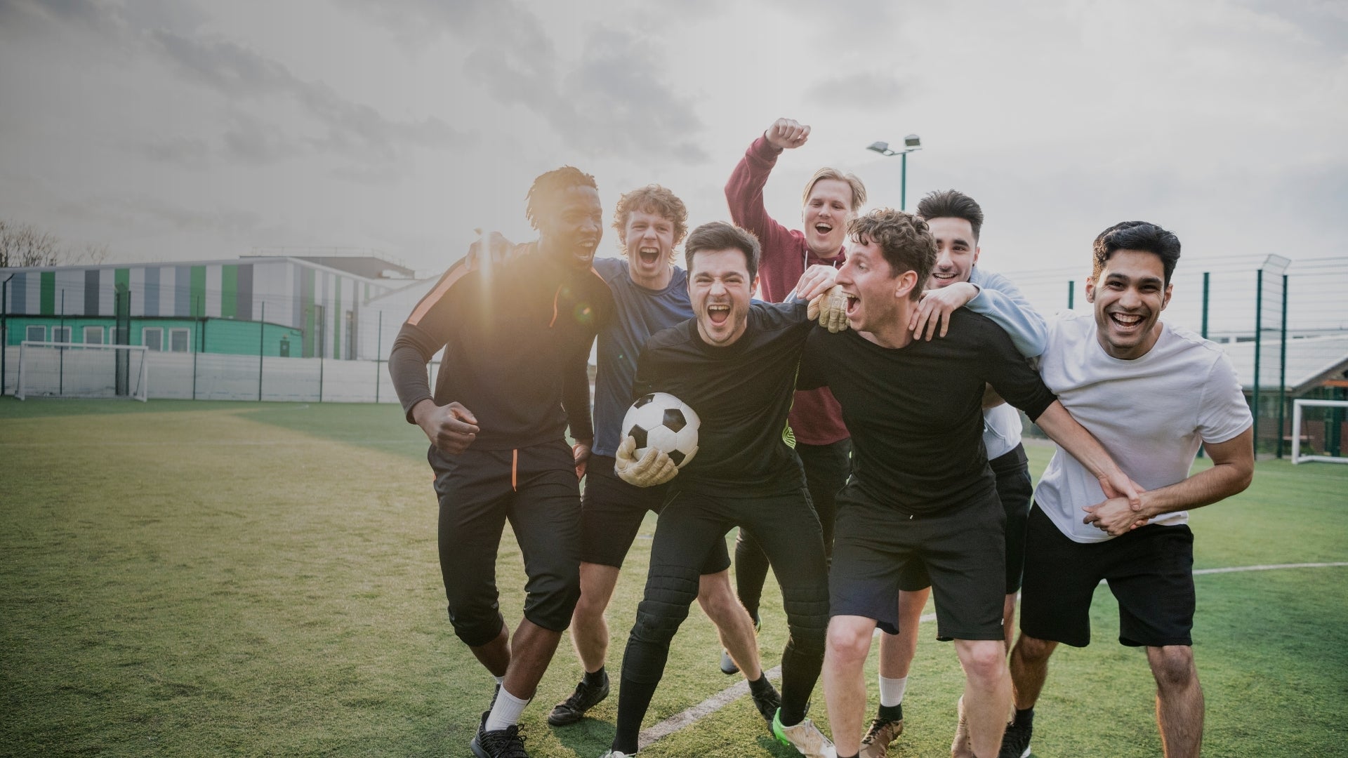 Group of young men celebrating on a soccer field with a soccer ball.