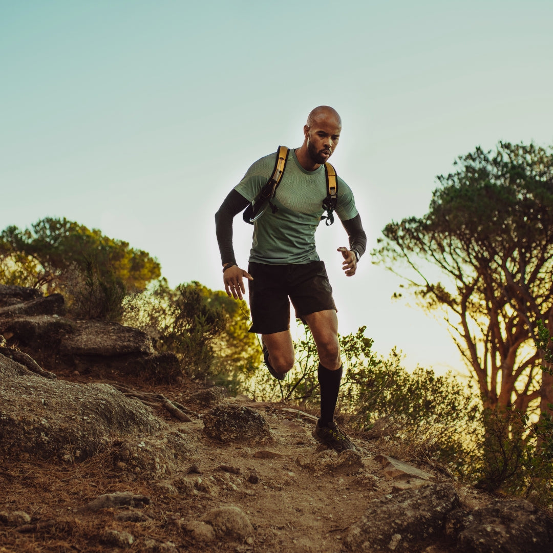 Athletic man in green shirt trail running uphill on rocky mountain path at sunset